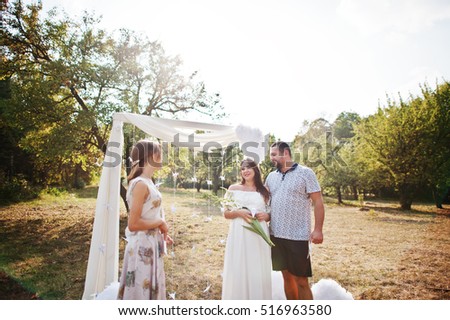 Man with pregnant woman and master of ceremony stay background white arch on garden