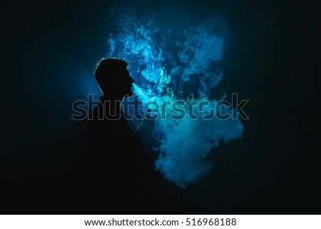 The young man smoke an electronic cigarette against the background of the blue light