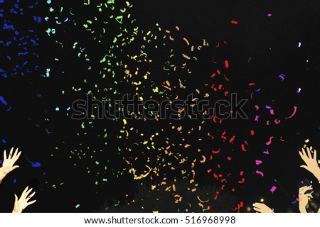 Rainbow confetti fired in the air during a beach party. Hands in the air on both sides of the pic