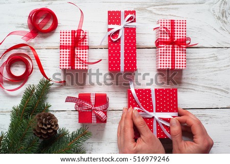 Christmas gift box.  Female hands wrapping Christmas red present box above white wooden table. Flat lay.