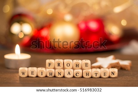 Frohe Weihnachten on cubes in foreground, decoration in the blurry background ; frohe weihnachten means merry christmas