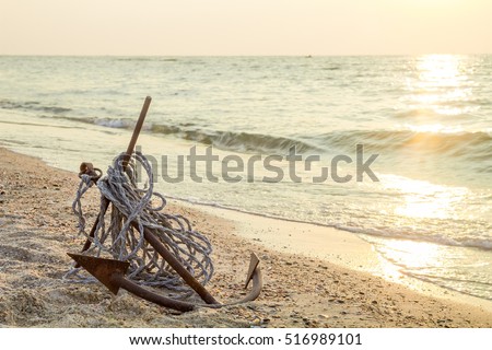 RUSTY ANCHOR WET BEACH SAND AND WHITE SEA-WAVE FOAM Royalty-Free Stock Photo #516989101