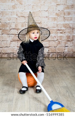 The child, a little girl in the image of the witch posing in a studio with a pumpkin and a broom on Halloween.