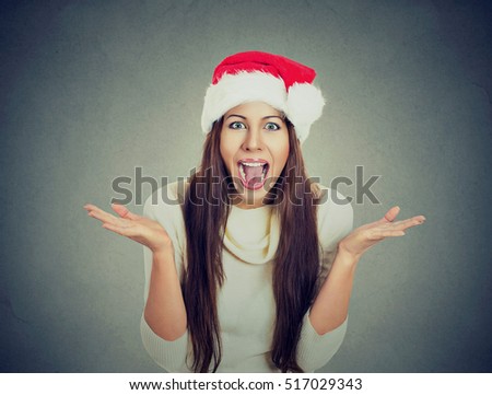 Surprised excited happy woman wearing red santa claus hat looking shocked by what she saw isolated gray background. Positive emotion