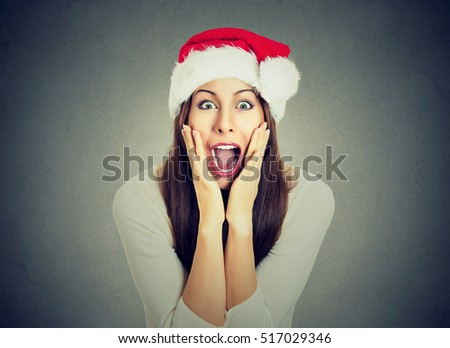 Surprised excited happy woman wearing red santa claus hat looking shocked by what she saw isolated gray background. Positive emotion