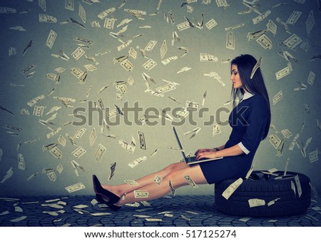 Young woman using a laptop building online business making dollar bills cash falling down. Beginner IT entrepreneur under money rain. Success economy concept