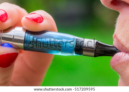 A close up view of a woman inhaling from an electronic cigarette outside.