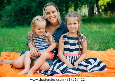 Mother with two daughters in striped clothing sitting on orange blanket in park. Happy parenting concept
