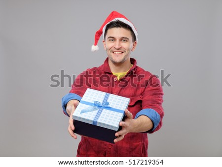 Handsome guy holding a gift and emotionally happy Christmas isolated on gray background