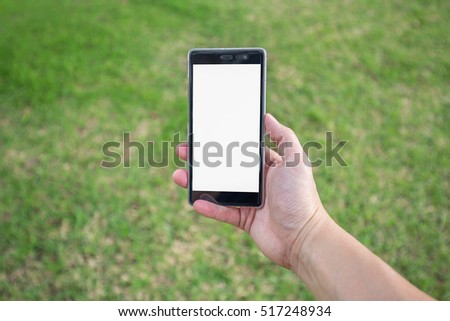 Man's right hand hold blank white screen mobile phone with blurry scene of green grass in park.