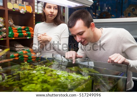 Young man and girl smiling and watching aquarium fish in shop