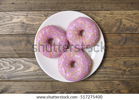 Aerial view of a plate of ring donuts with pastel pink frosting and sprinkles on a rustic wooden table background