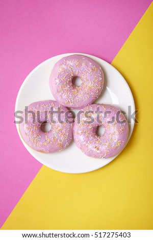 A plate of ring donuts with pastel frosting and sprinkles on a pink and yellow background