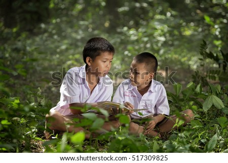 Young asian boy reading book to each other in the woods, countryside of thailand