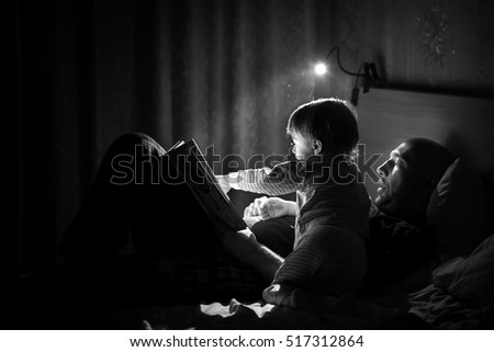 Dad is reading a bedtime story to his little son. Night lamp is shine beautifully. Black and white image with selective focus.