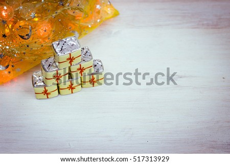Little Chocolate Sweets in a Form of Gift Boxes on Wooden Texture with Christmas Lights. Holiday background. Merry Christmas and a Happy New Year Card with Space for Text.