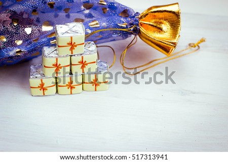 Little Chocolate Sweets in a Form of Gift Boxes on Wooden Texture with Gift Bag. Holiday background. Merry Christmas and a Happy New Year Card with Space for Text.