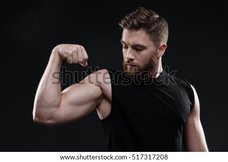 Fitness man demonstrates bicep. looking at bicep. in studio. isolated dark background