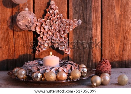 Christmas scene, winter composition with lit white candle, golden mini glass balls on vintage silver color metal plate, cedar cone, wooden star with tinsel on dark weathered background, evening light 