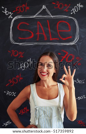 Young woman is showing ok sign with her hand while posing against blackboard with chalk sale advertisement