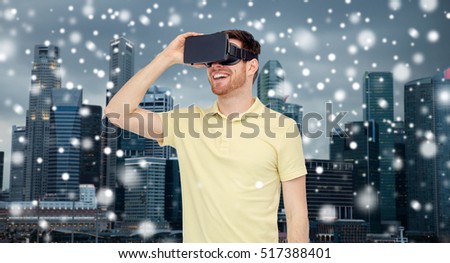 technology, augmented reality, winter, christmas and people concept - happy young man with virtual headset or 3d glasses over singapore city skyscrapers background and snow