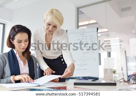 Mature businesswoman with female colleague reviewing project at desk in office