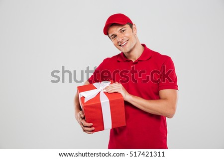 Smiling delivery man with christmas gift in studio. looking at camera. isolated gray background