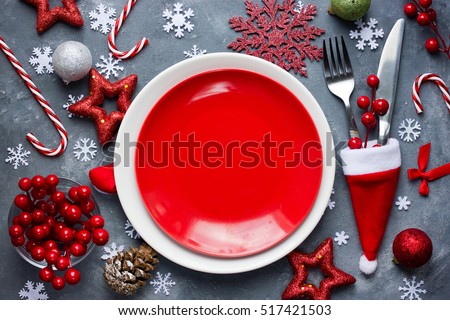 Christmas table place setting with empty red plate, cutlery in santa hat with festive decorations bauble snowflake star bow ball pinecone berry candy cane. Christmas Xmas New Year holiday background