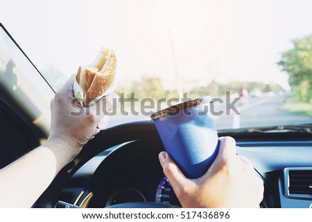 Man is dangerously eating hot dog and cold drink while driving a car Royalty-Free Stock Photo #517436896