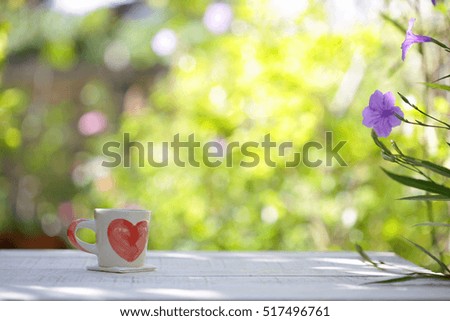 White cup whit heart pattern and plants on wooden table