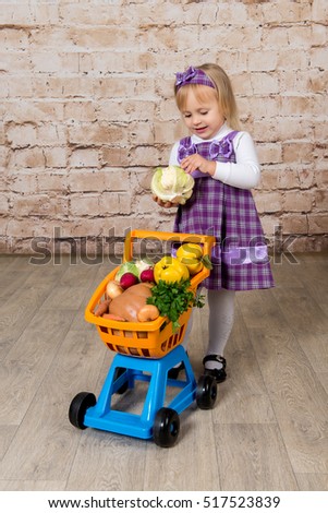 The child, a little girl with a cart full of vegetables and fruits. Purchase of products in the supermarket.