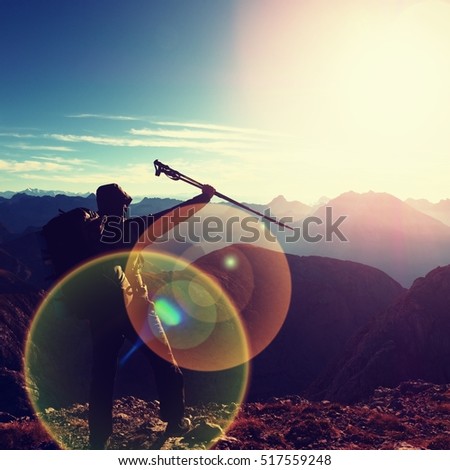 Lens flare light, strong defect. Happy alone adult backpacker with raised poles, hands in the air. Open view to Alpine mountain, amazing day in nature. 