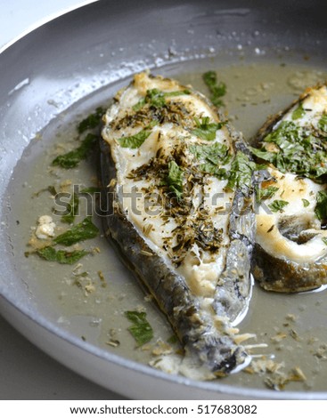Roaster trout steaks with parsley and other herbs on a pan over a white background