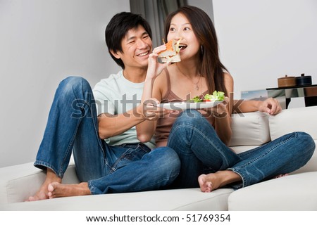 A good looking couple having a sandwich on their couch at home