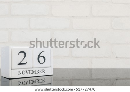 Closeup white wooden calendar with black 26 november word on black glass table and white brick wall textured background with copy space , selective focus at the calendar