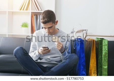male young with the phone mobile and the card of credit in the sofa of house