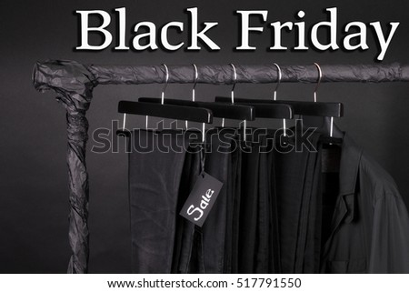 A lot of black pants jeans and jacket hanging on clothes rack. Black background. sale sign. Black friday. Close up.