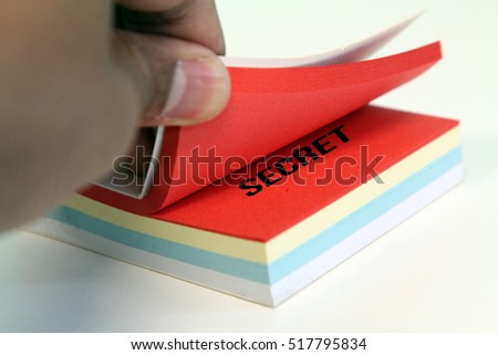 A conceptual image of a hand peel taking a colored stick post-it note isolated white background with a word Secret