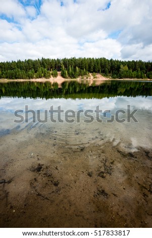 calm lake with reflections of clouds in summer with forest in background