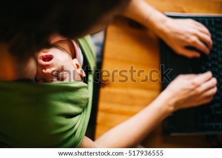 Mother Working From Home With Newborn Baby Sleeping ni Wrap Carrier Typing on Laptop Computer 