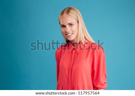 Portrait of a happy smiling blonde girl in red dress looking at camera isolated on a blue background