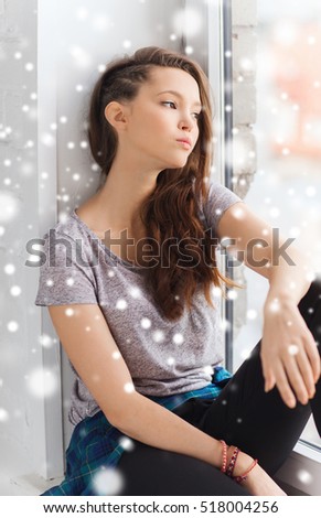 people, winter, christmas and teens concept - sad unhappy pretty teenage girl looking through window over snow