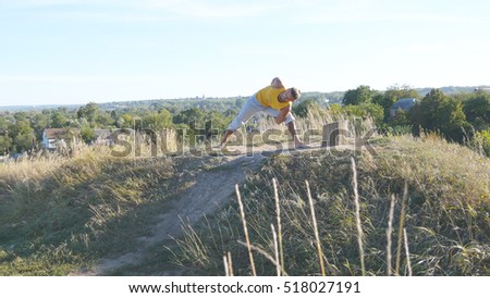 Young man standing at yoga pose at nature. Guy practicing yoga moves and positions outdoors. Athlete doing strength exercise at the hill. Landscape at background. Healthy active lifestyle. Close up