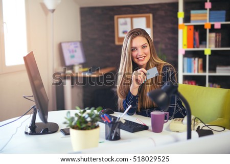 Businesswoman sitting at desk in office and holding credit card