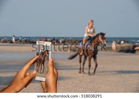 Hand of photographer with smart phone shooting image on blurred a girl riding on the beach    background