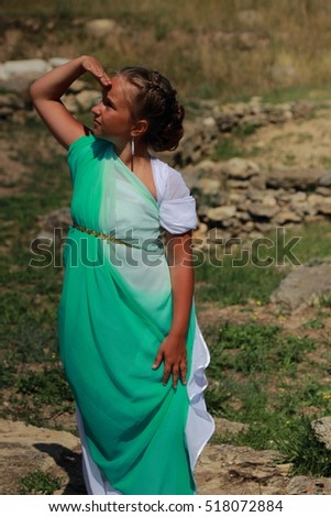 Adorable little girl in a green tunic in antique style on a background of ruins of the ancient city