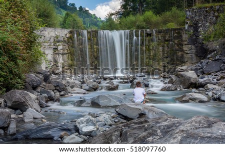 Child Seating on rocks in front of a waterfall 