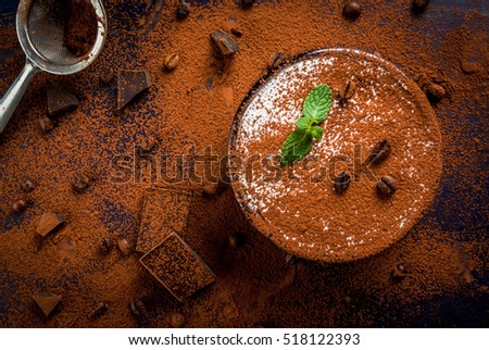 Traditional Italian dessert tiramisu decorated with cocoa and mint leaves. On a dark blue wooden table, decorated with cocoa, dark chocolate, coffee beans and mint leaves. Copy space, top view