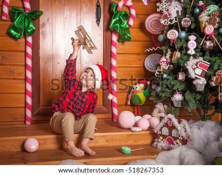Boy in a plaid shirt and suspenders near the Christmas tree. the New Year with gifts under the Christmas tree and the fireplace. child playing with toy airplane. the dream of becoming a pilot