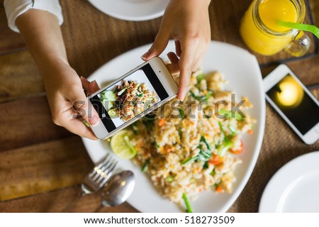 Hands with the phone close-up pictures of food. Fried rice with chicken and mango shake, one dish for two. Royalty-Free Stock Photo #518273509